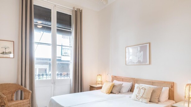 Una camera da letto con un letto grande, una sedia in vimini, due comodini con lampade e vista su un balcone.
