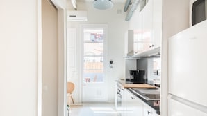 Una cucina stretta con mobili bianchi, un piano di lavoro nero e un frigorifero bianco.