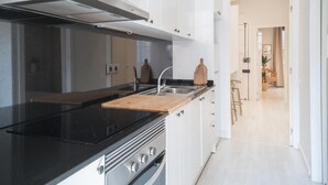 Una cucina moderna con piano cottura nero, lavello in acciaio inossidabile e pensili bianchi. Sul ripiano si trova un tagliere di legno.