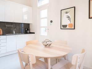 A modern kitchen with white cabinets, a black countertop, and a round wooden table with chairs. - Light, cozy terrace and local life in Gracia (Barcelona)