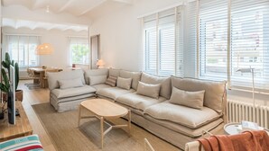 A spacious living room with a large L-shaped sofa, a wooden coffee table, and a dining area in the background.