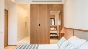 A bedroom with a bed, a wooden wardrobe, a bathroom with a sink, and a shower.