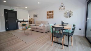 Ein modernes Wohnzimmer mit einer Couch, einem Esstisch mit Stühlen, einem Teppich und Wandbildern.