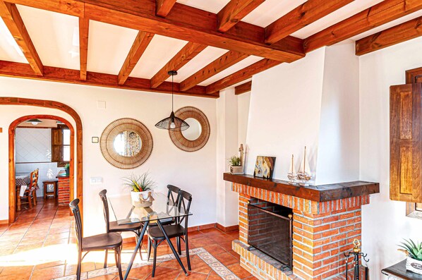 A room with a fireplace, wooden beams, a dining area with chairs, and a mirror on the wall. - Sabina's house (Llanes)