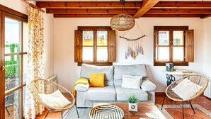 Una sala de estar acogedora con un sofá gris, dos sillones de mimbre, una lámpara colgante de fibra natural y una mesita con una planta.