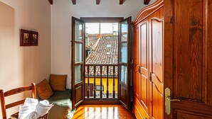 Una habitación con una puerta de madera, una ventana que da a un tejado de baldosas, un banco de madera y una mesita con ropa doblada.