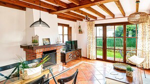 Amplia sala de estar con chimenea, televisor y comedor con vistas al jardín.