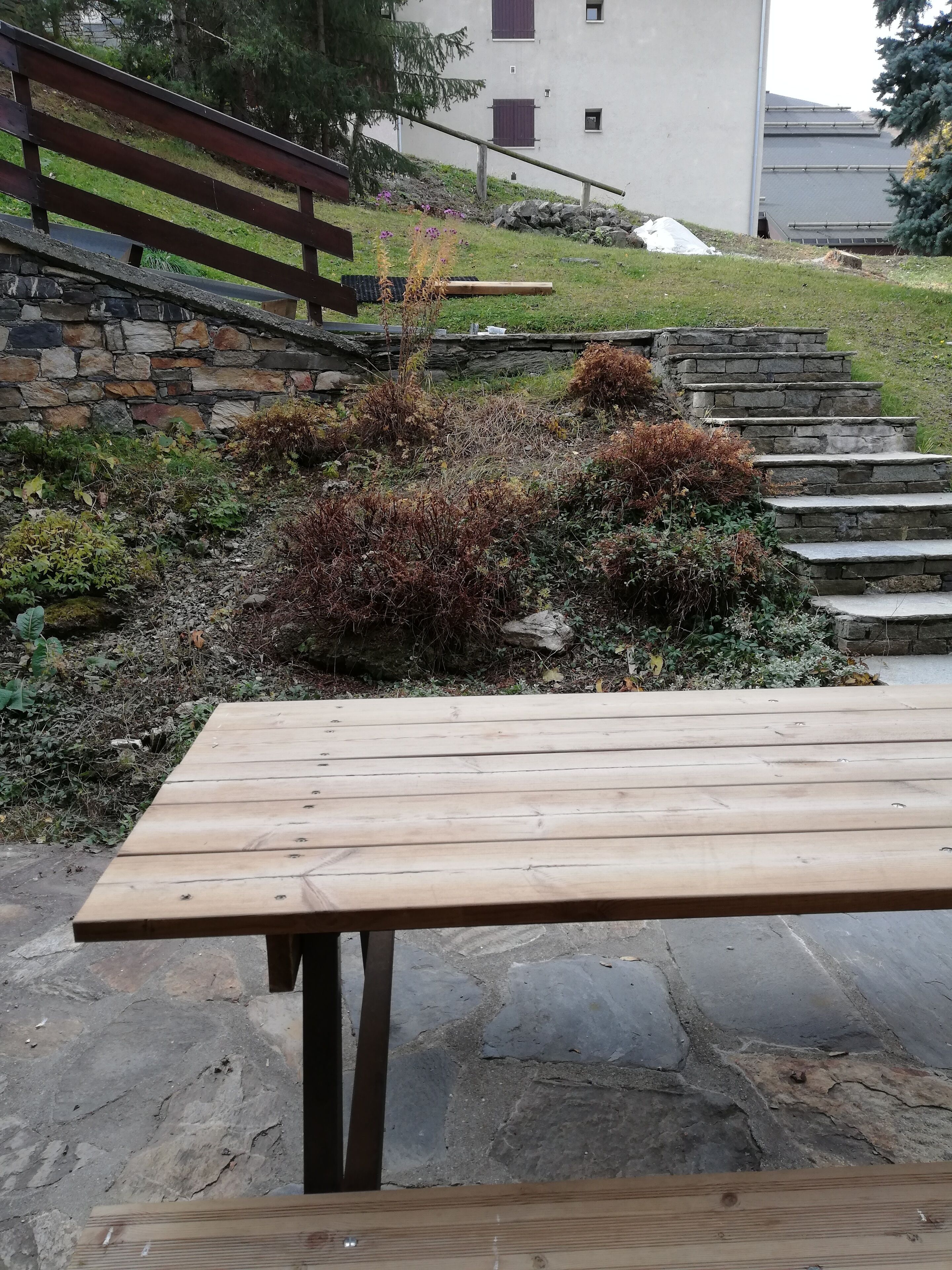 Ein Holztisch für ein Picknick auf einem gepflasterten Steinplatz mit einer Steintreppe und einem Gebäude im Hintergrund.