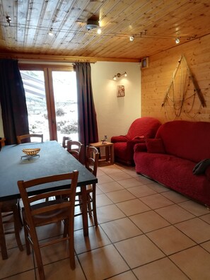 Interior de madeira com uma mesa de jantar, cadeiras, um sofá vermelho e uma pequena mesa com uma cesta.