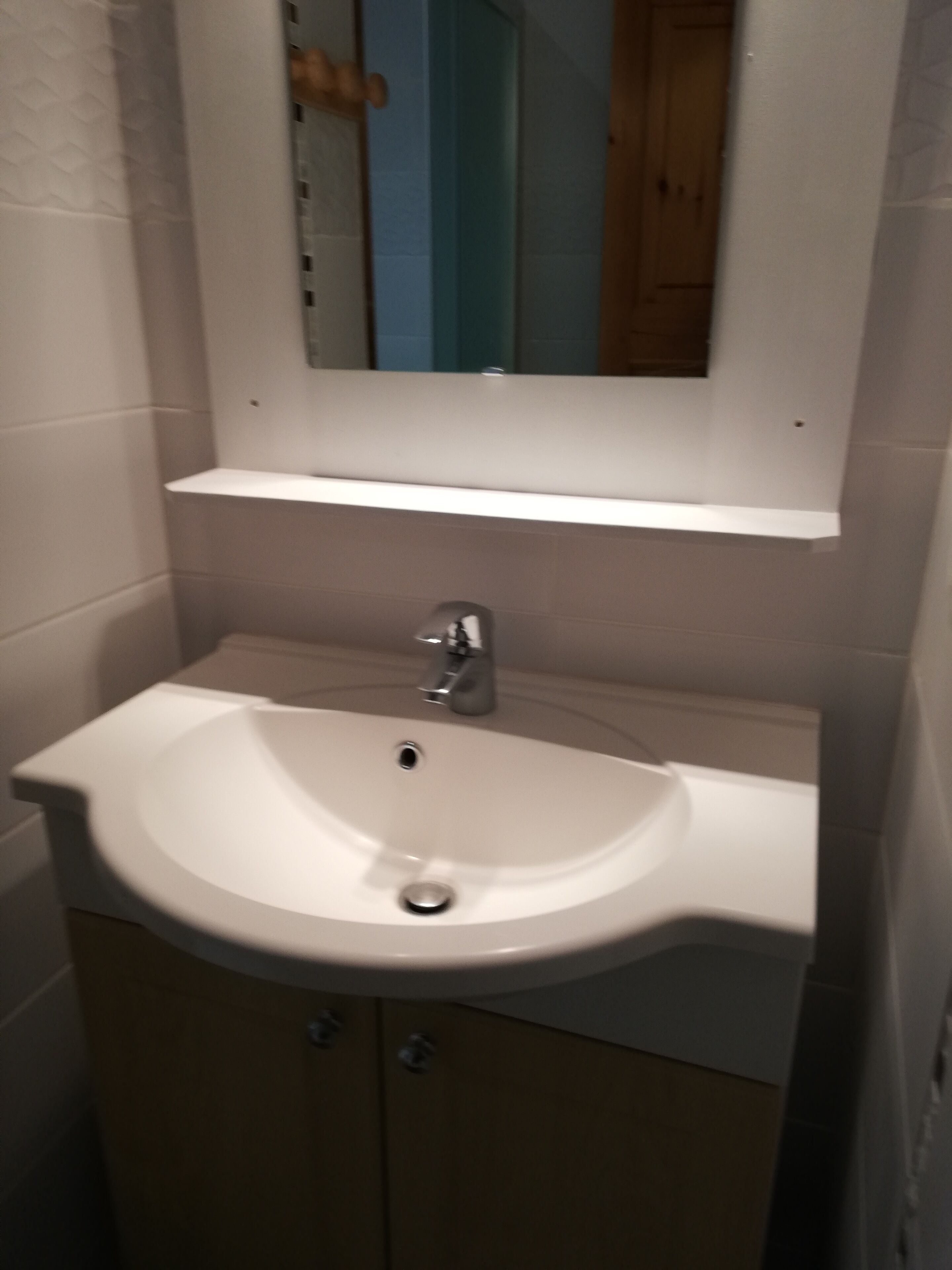A bathroom with a white sink, a mirror above it, and a wooden cabinet below.