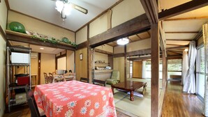 Een traditionele Japanse kamer met tatami vloeren, een houten tafel met een tafelkleed met bloemenmotieven en zicht door een shoji scherm op een andere kamer.