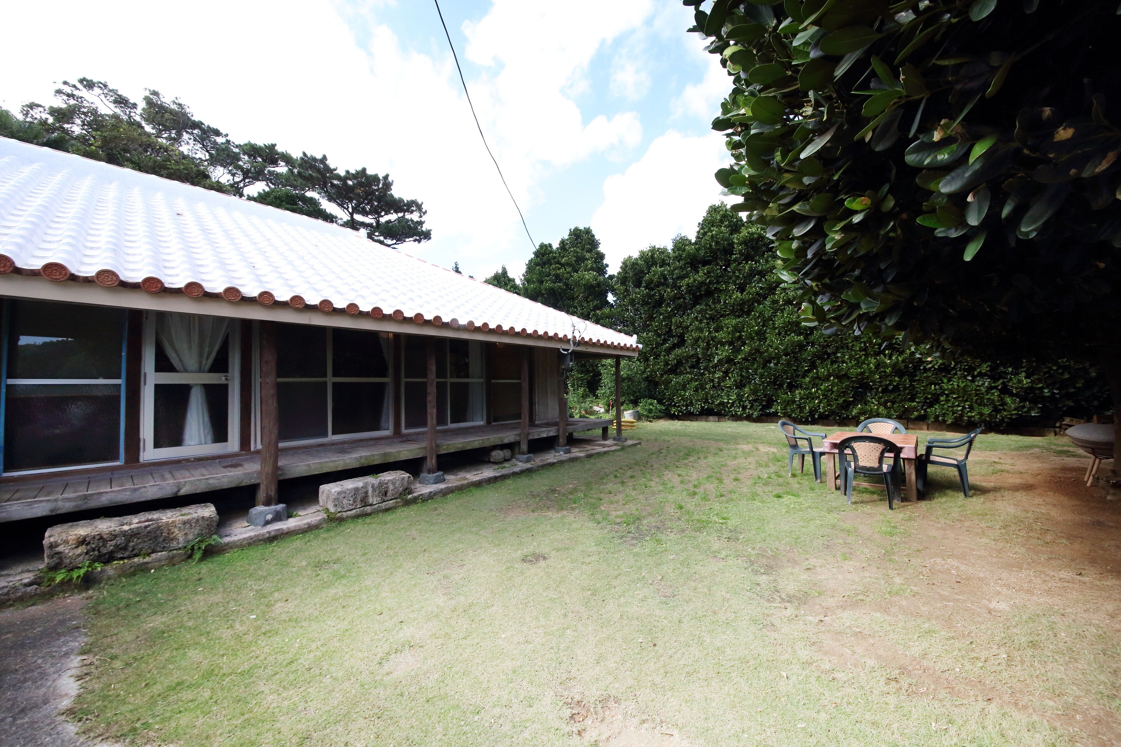 A covered outdoor seating area with a table and chairs, a wooden deck, and a grassy lawn.