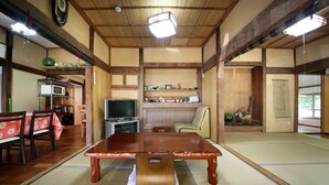 Een traditionele Japanse kamer met tatami vloerbedekking, een houten eettafel en een televisie.