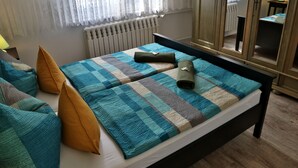 Ein ordentlich bezogenes Bett mit kariertem Überwurf und Kissen, ein Heizkörper, ein Spiegel und eine Lampe auf einem Nachttisch.