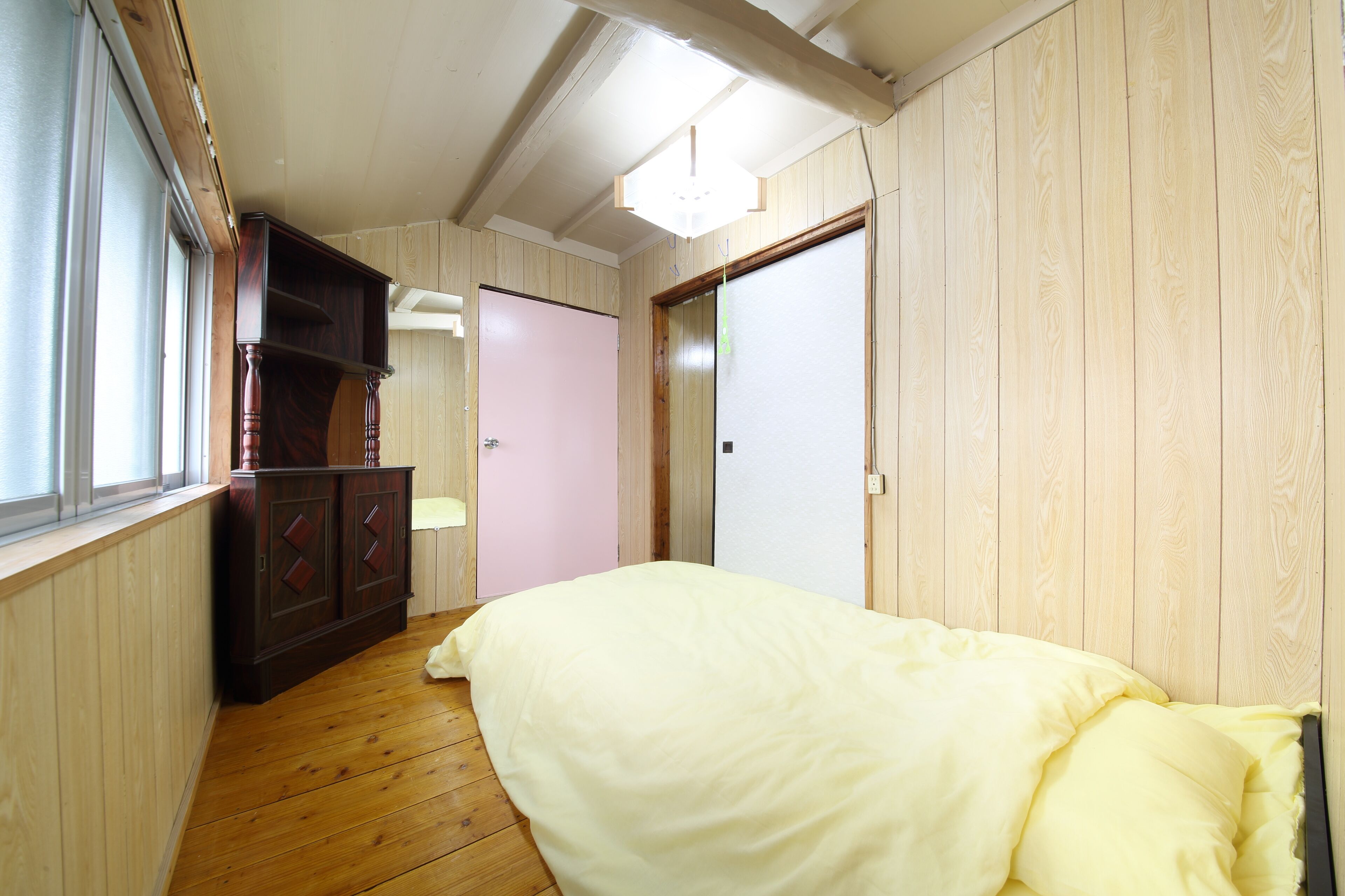 A bedroom with a wooden floor, a bed with a white duvet, a wardrobe, a door, and a window.