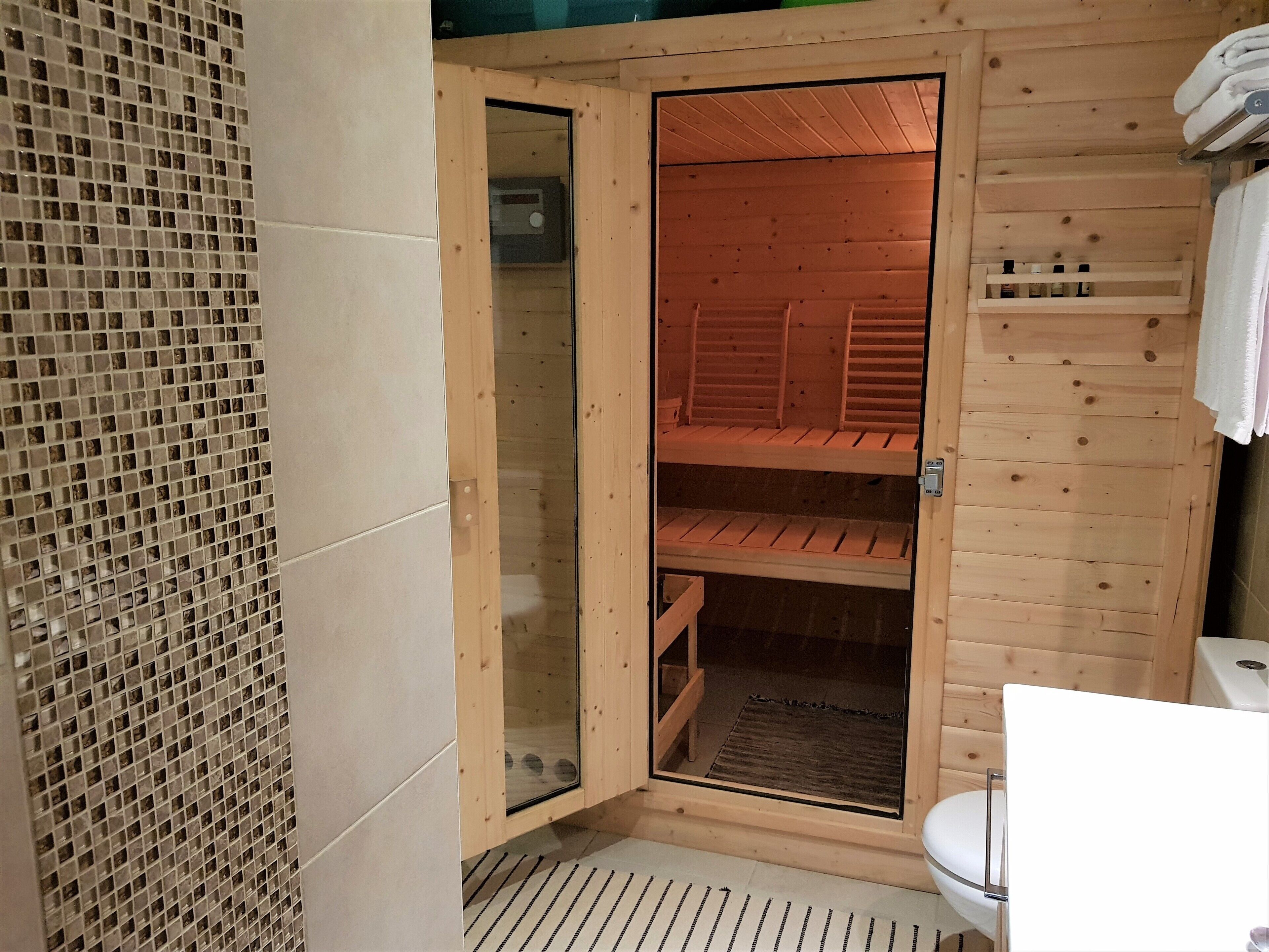 A wooden sauna with glass doors, a tiled floor, and a white toilet.