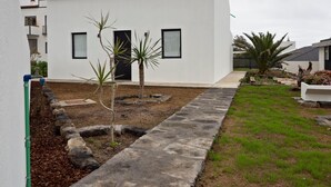 A modern building with a flat roof, a small garden area with young trees, and a paved walkway.