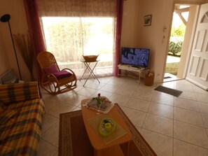 A living room with a sofa, a chair, a coffee table, a television, and a window with curtains.