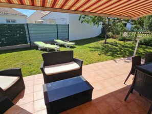 An outdoor patio area with wicker furniture, a covered section, and a lawn with sun loungers. - Single-storey house between beaches and shops (Vaux-sur-Mer)