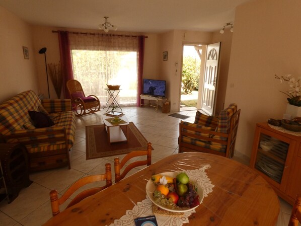 A living room with a sofa, chairs, a coffee table, a TV, and a dining table with fruit.