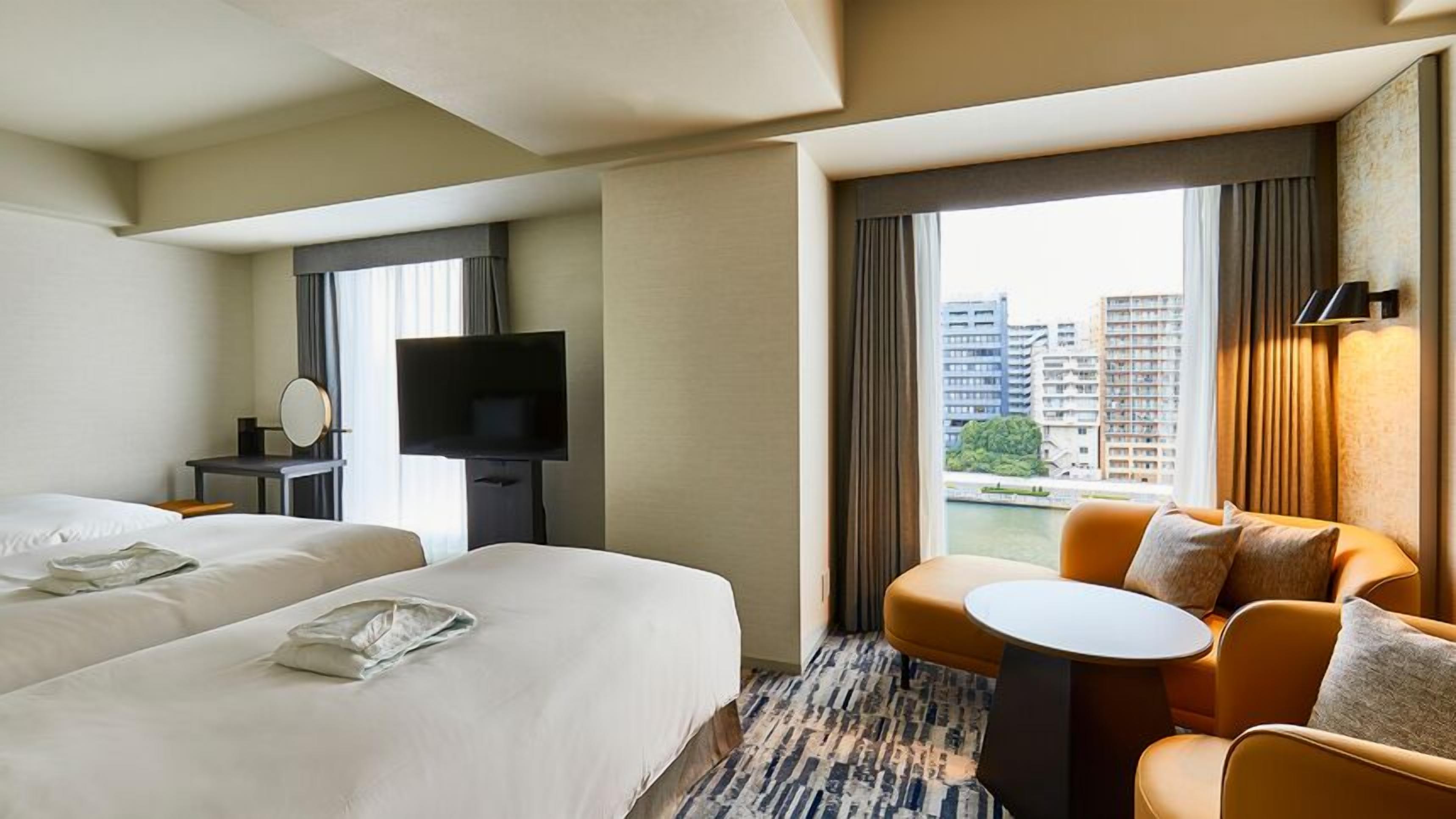 Een hotelkamer met twee bedden, een televisie, een tafeltje en uitzicht op gebouwen.