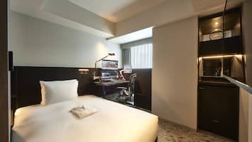 A hotel room with a large bed, a desk with a computer, a chair, and a small kitchenette.
