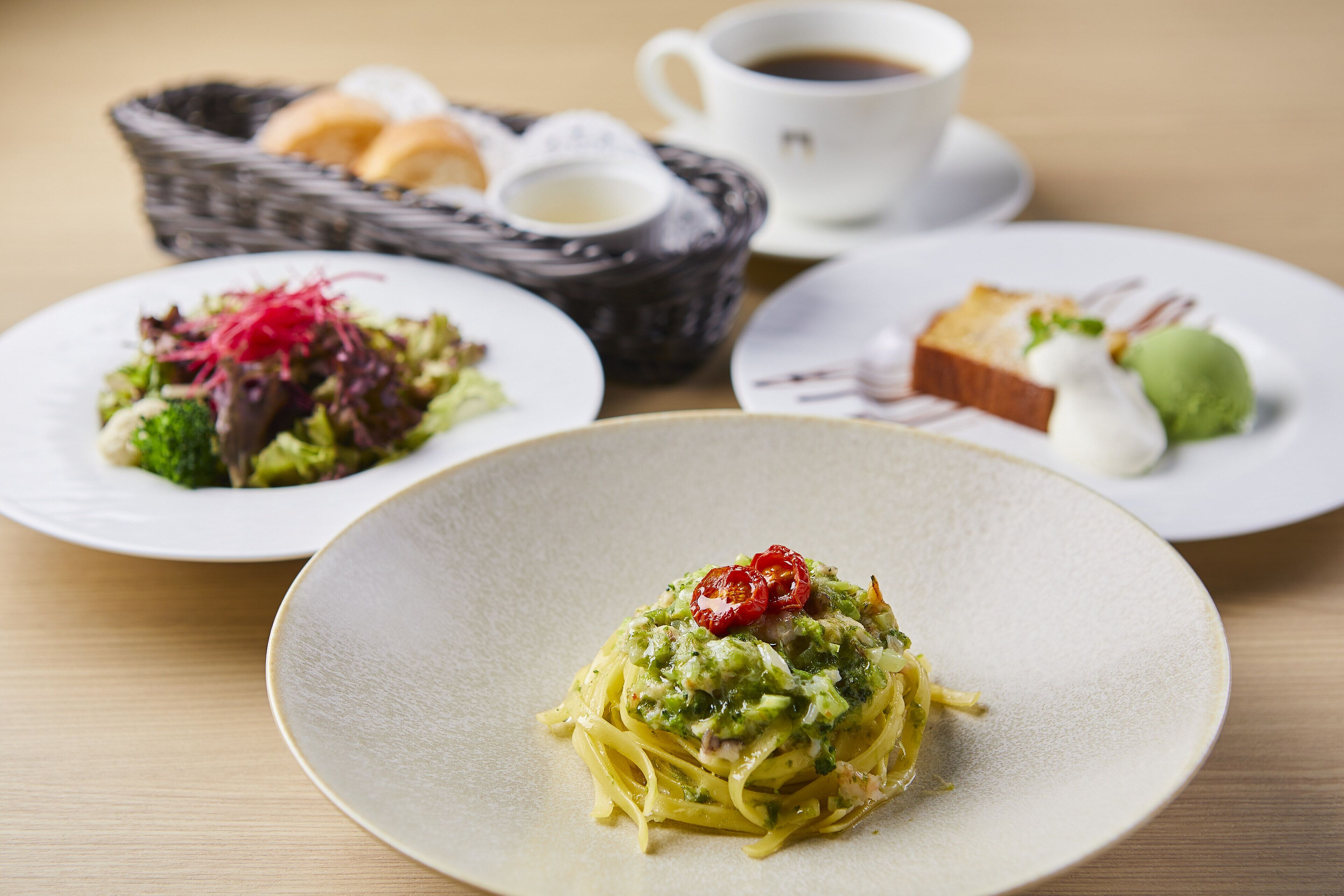 A table with three plates of food, a cup of coffee, and a basket of bread.