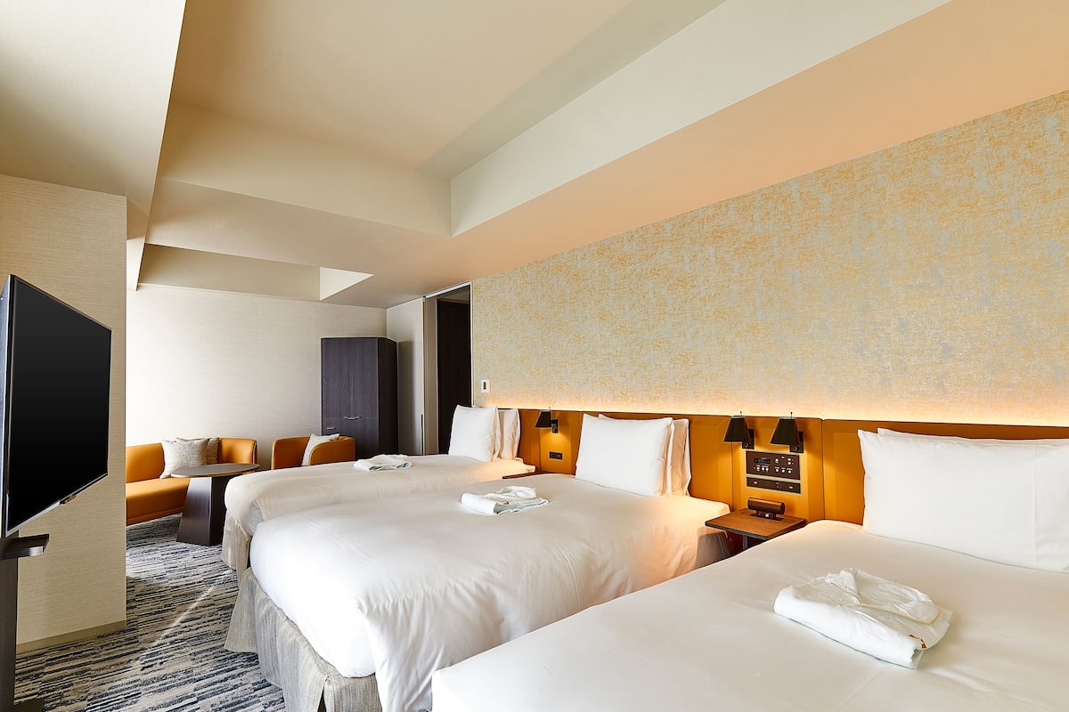 A hotel room with two beds, a sofa, a TV, and a desk.