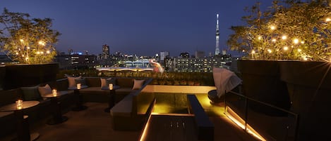 An outdoor seating area with tables and chairs, a grassy patch, and a view of a city skyline including a tall tower.