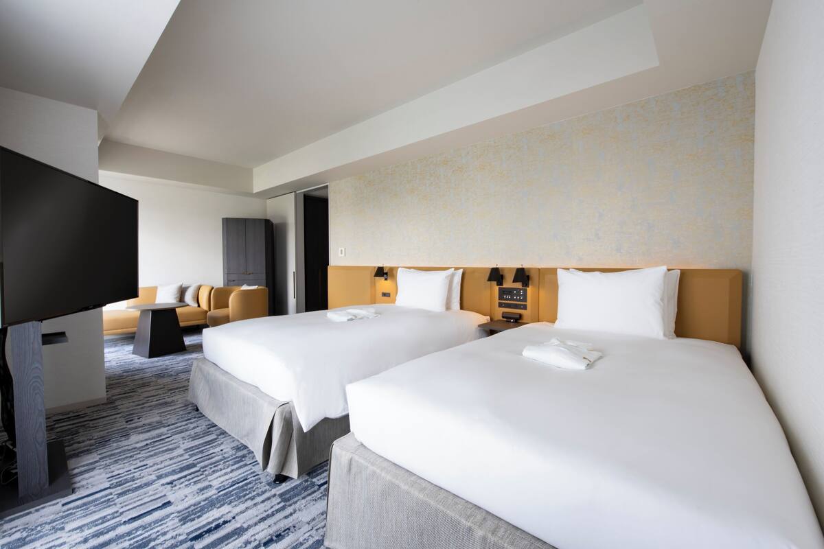 A hotel room with two beds, a flat-screen TV, a sofa, and a carpeted floor.