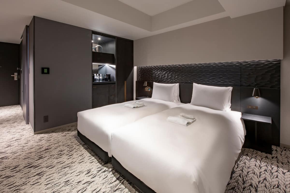 A modern hotel room with a large bed, a built-in wardrobe, and a seating area with a table and chairs.