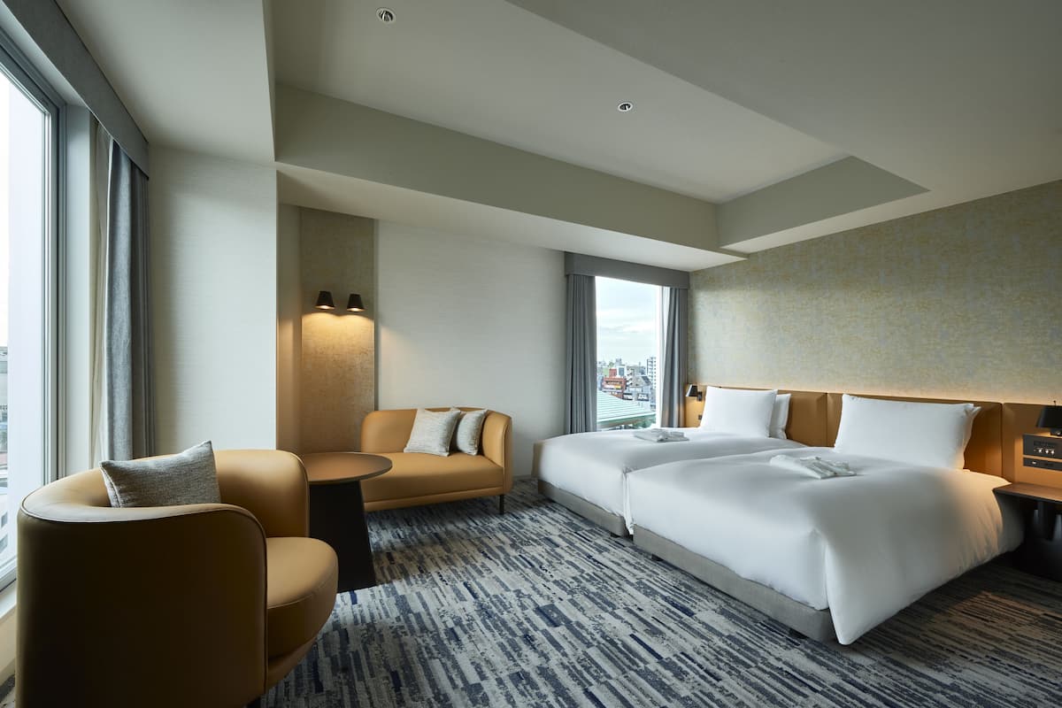 A hotel room with a large bed, a sofa, a small table, and a view of the city.