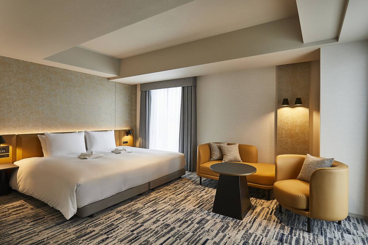 A hotel room with a large bed, a sofa, a small table, and a lamp.