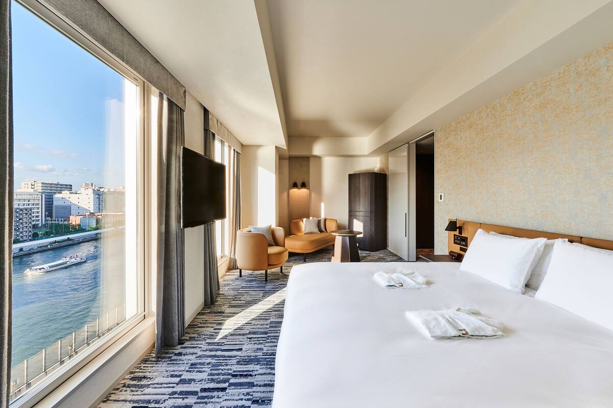 A hotel room with a large bed, a seating area with chairs, a television, and a view of a river.