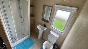 Un baño pequeño con ducha, lavamanos, inodoro y ventana.