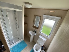 A compact bathroom with a shower, sink, toilet, and a window. - 3 Bed 8 Berth Caravan in California Cliffs - D53 (Great Yarmouth)