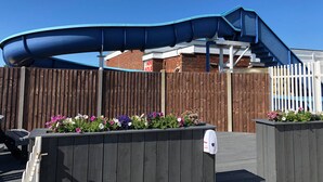 A playground with a blue slide and a wooden fence. - 3 Bed 8 Berth Caravan in California Cliffs - D53 (Great Yarmouth)