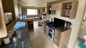 A compact RV kitchen with a stove, sink, and wooden cabinets. - 3 Bed 8 Berth Caravan in California Cliffs - D53 (Great Yarmouth)