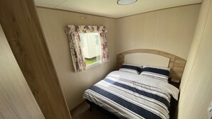 Un dormitorio pequeño y acogedor con una cama individual, una ventana con cortinas florales y un cabecero de madera.