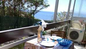 Ein sonniger Essbereich im Freien mit einem Tisch für zwei Personen, einem gepolsterten Stuhl und Blick aufs Meer.