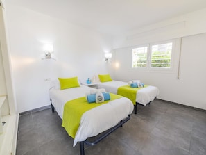 Ein Hotelzimmer mit zwei Betten, jeweils mit grüner Bettdecke und weißer Bettwäsche, einem kleinen Tisch mit einer Wasserflasche und einem Fenster mit Blick auf Grünflächen.