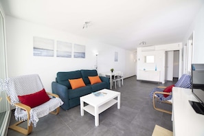 A modern living room with a sofa, a rocking chair, a coffee table, and a dining area. - Apartamento Beachfront Sonrisas (Puerto de Alcudia)