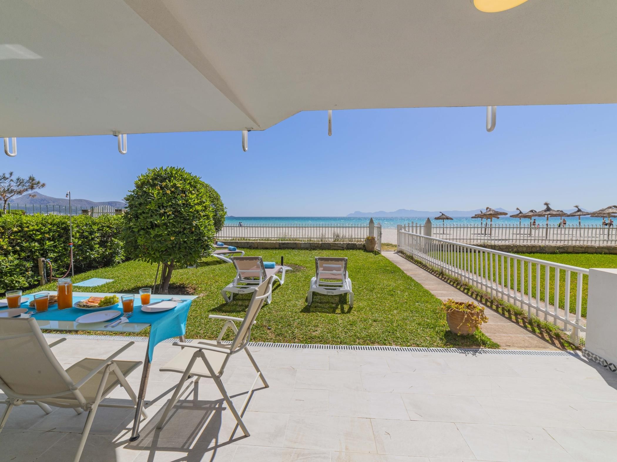 Eine Terrasse mit Frühstückstisch, Lounge-Sesseln und Blick auf Strand und Meer.