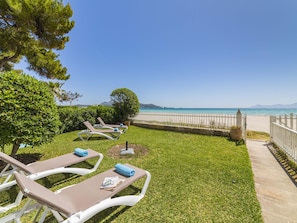A seaside resort with lounge chairs, a grassy lawn, and a view of the ocean. - Your long term rental beachfront apartment in Puerto de Alcúdia. (Puerto de Alcudia)