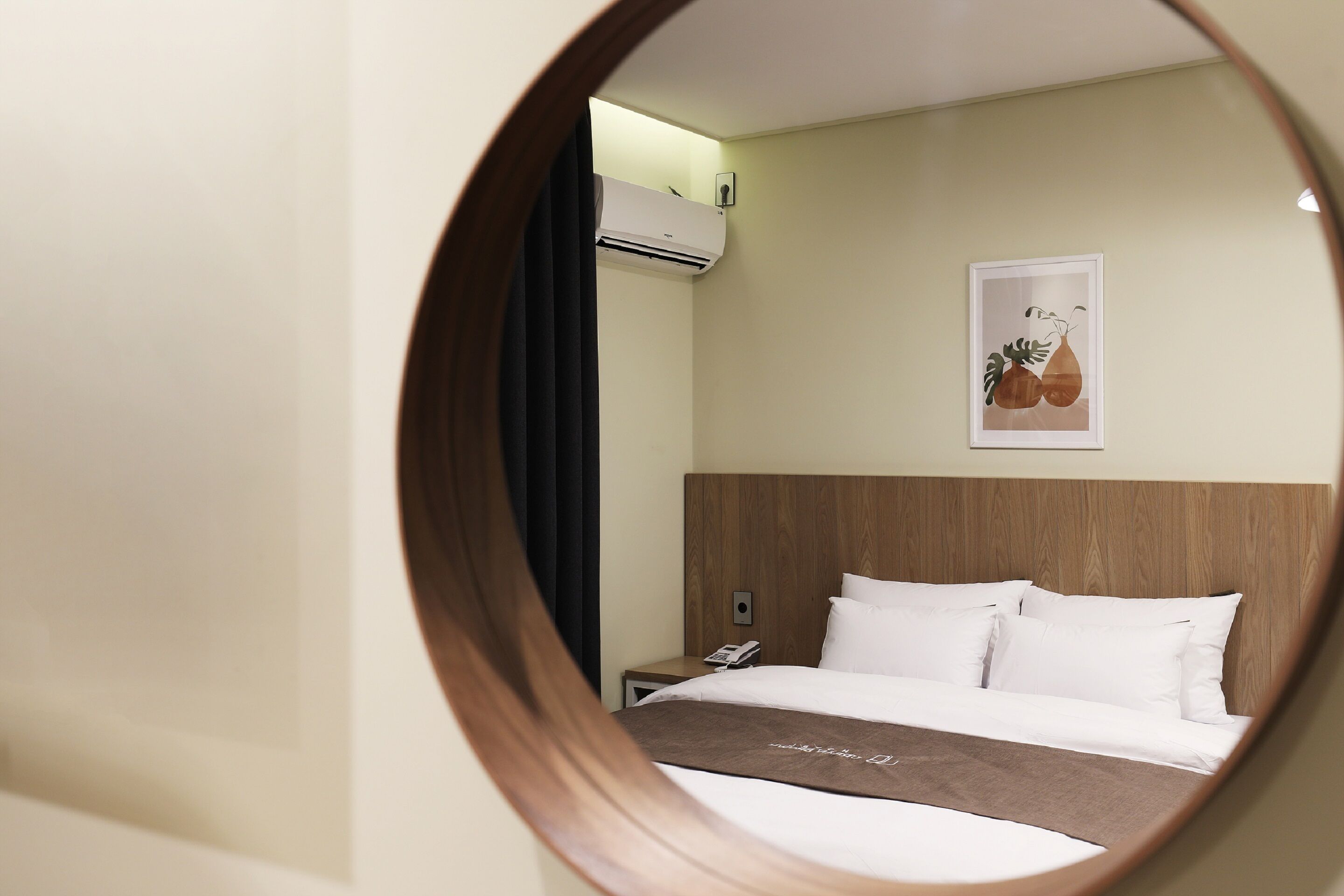 Habitación de hotel con cama, mesita de noche con teléfono, aire acondicionado y un cuadro en la pared.