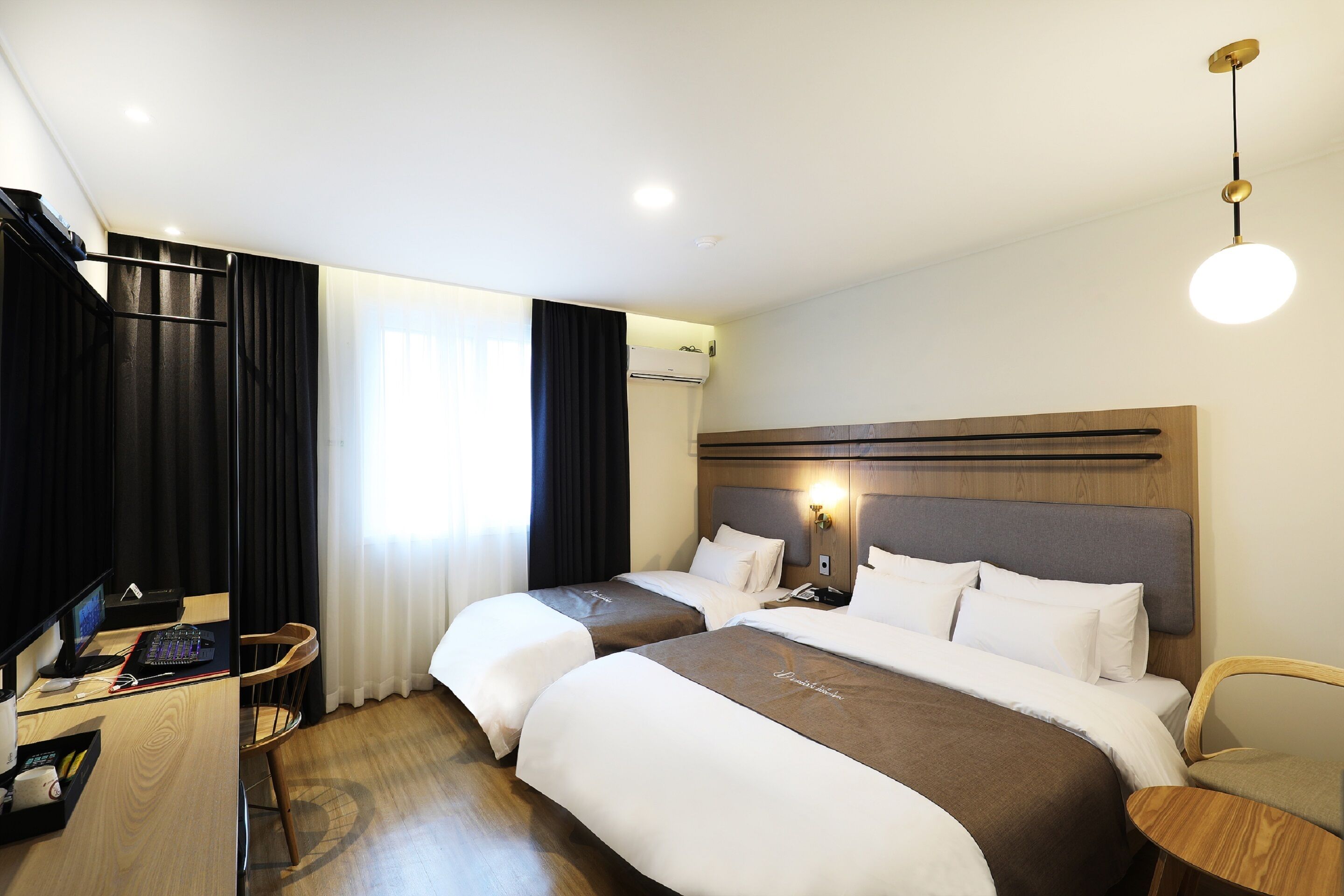 A hotel room with two beds, a desk with a computer, a chair, and a bedside table.