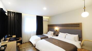 A hotel room with two beds, a desk with a computer, a chair, and a bedside table.