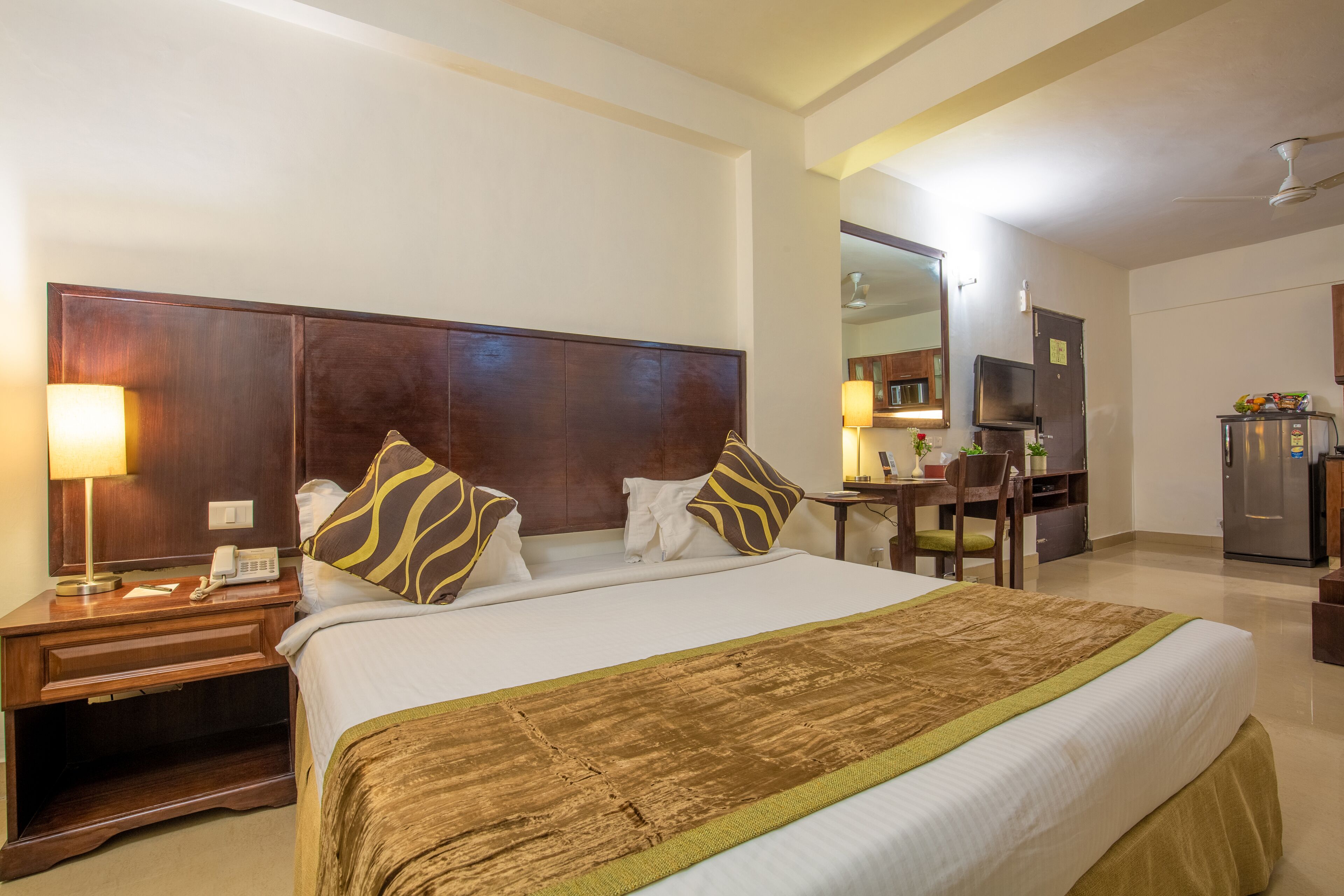 Una habitación de hotel con una cama grande, un escritorio con silla, un televisor y un refrigerador.