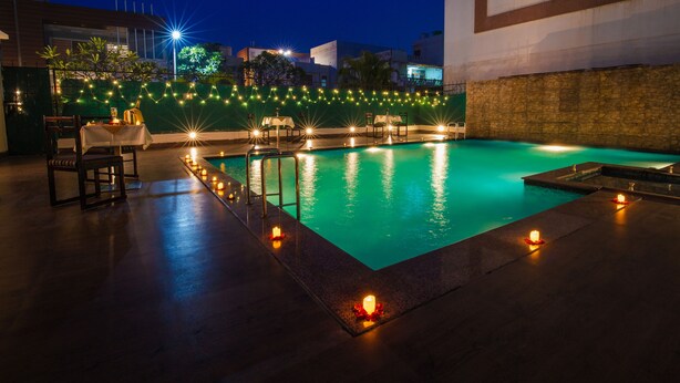 Una piscina con una pared de piedra y una mesa con sillas, rodeada de luces colgantes.