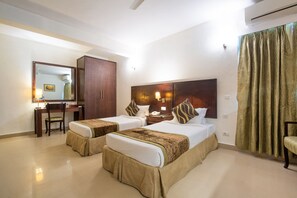 A hotel room with two beds, a desk, a chair, a wardrobe, and a large mirror. - Rosewood Apartment Hotel - Pantnagar (Kichha)